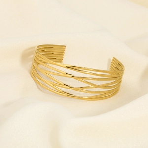 Detail of a layered gold-plated stainless steel cuff bracelet on beige fabric