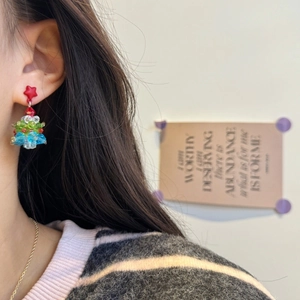 Close-up of handmade beaded Christmas tree earrings with a red star on a model's ear