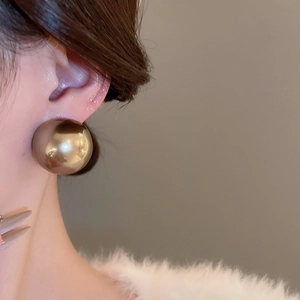 Gros plan d'une grande boucle d'oreille sphérique dorée minimaliste sur un mannequin