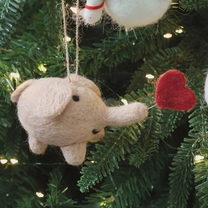 Cute pink wool felt elephant ornament with red heart on a decorated Christmas tree