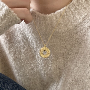 Detail of a textured golden sunburst pendant necklace worn over a beige sweater