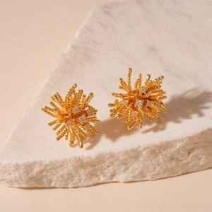 Gros plan de boucles d'oreilles feu d'artifice dorées avec zircons sur pierre
