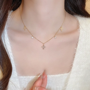 Close-up of a gold cross necklace with zircon charms on a model's neck for elegant daily wear