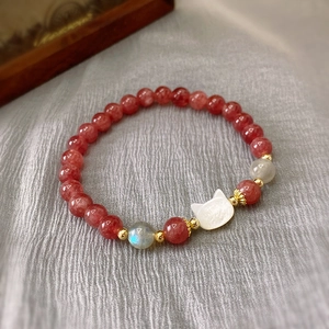 Macro view of strawberry quartz beads and white shell cat pendant on a handmade bracelet