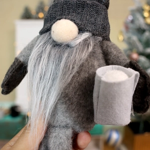 Close-up of grey felt Christmas gnome ornament with white faux fur beard and festive background