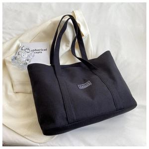Detail of black canvas tote bag featuring a white minimalist label on neutral background