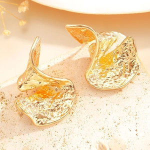 Close-up of golden wavy hammered earrings with textured surface on natural stone