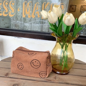 Brown corduroy cosmetic bag with smile prints on a rustic wooden table with tulips
