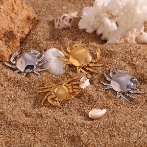 Detail of crab-shaped 18K gold and silver earrings on sand with shells and coral