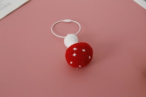 Macro detail of handmade crochet mushroom keychain with red cap and white dots on pink background