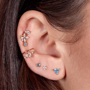 Close-up of gold S925 silver ear studs with blue and clear crystals on a model's ear