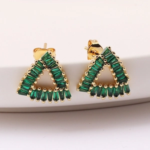 Detail of triangle gold earrings with emerald green zircon on a white ceramic plate