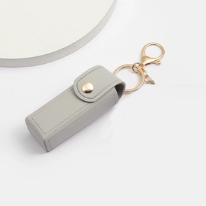 Close-up of grey pebble leather lipstick keychain bag with gold hardware and snap button