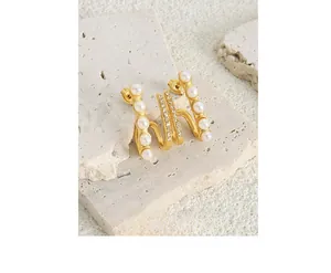 Detailed view of wavy gold earrings with imitation pearls and crystals on stone background