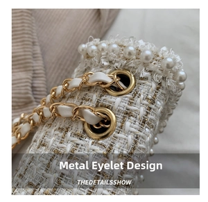 Close-up of elegant tweed fabric with pearl trim and gold chain eyelet hardware details