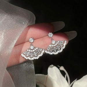 Macro shot of fan-shaped silver earrings with cubic zirconia held by hand