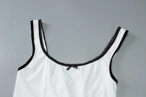 Détail d'un haut blanc à col en U avec bordure en dentelle noire et petit nœud central
