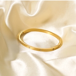 Dettaglio del bracciale rigido in acciaio dorato con finitura spazzolata e zirconi a stella