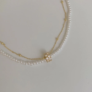 Détail d'un collier de perles double couche avec pendentif cylindre doré serti de zircons