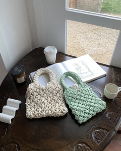 Hand-woven cream and mint green knit handbags with drawstring liner on a wooden table