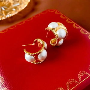 Macro view of vintage gold-plated C-shape earrings featuring white pearls and bead edges