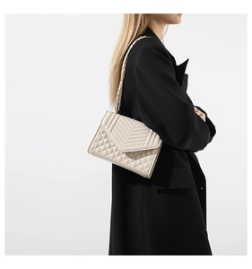 Detail of beige quilted shoulder bag with V-shaped texture and gold chain on black blazer