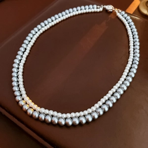Detail of double-layer necklace with white and silver-grey pearls on leather background