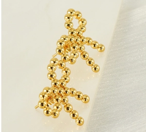 Macro shot of 18k gold plated stainless steel beaded bow earrings on marble and silk