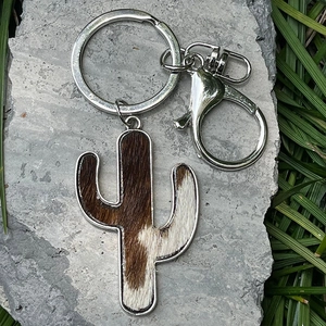 Western cactus keychain with cowhide print in a silver metal frame on stone background