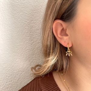 Detailed view of gold evil eye earring with blue stone and hanging zircon crystals