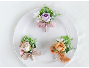 Detailed set of artificial rose boutonnieres in purple, champagne, and orange on a white plate