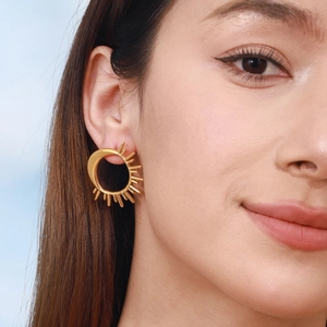 Elegant 18K gold-plated sun-shaped stud earrings worn by a model against a blue sky