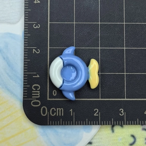 Detailed macro view of an 1.8cm blue and white fish resin charm on a scale ruler