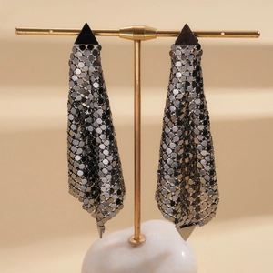 Detailed view of silver mesh fringe earrings with black triangle motifs on a gold stand