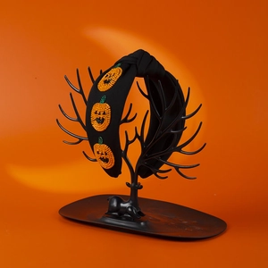 Halloween black fabric headband with orange beaded pumpkin embroidery on a display stand