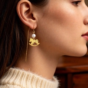 Close-up of golden rocking horse pendant with pearl on a long tassel threader earring