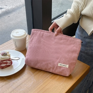 Pink corduroy makeup bag with striped texture shown in a cozy lifestyle cafe setting