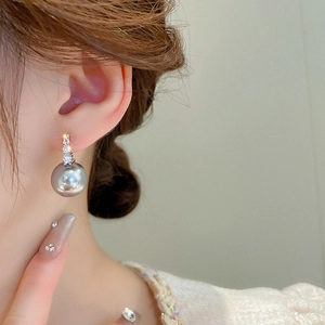 Close-up of a silver-toned earring featuring a grey pearl and zircon accents on a model