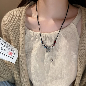 Close-up of ethnic style braided rope necklace featuring metal butterfly pendant and beads