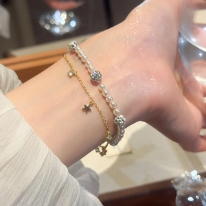 Detail of double-layer bracelet with pearls, gold star charm and zircon accents on wrist