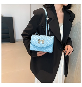 Detail of light blue quilted crossbody bag featuring silver metal bow and chain strap