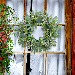 Artificial eucalyptus berry wreath hanging on a rustic wooden window with white curtains