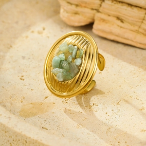 Macro detail of gold textured ring band with natural green stone on beige stone surface