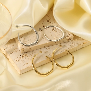 Irregular C-shape hoop earrings in 18k gold and silver finish on a stone display