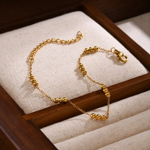 Detail of adjustable golden bead chain bracelet displayed on a wooden jewelry tray