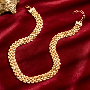 Macro detail of golden woven chain necklace with lobster clasp on red velvet backdrop
