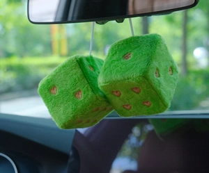Close-up of green plush dice with golden heart embroidery hanging in a car interior