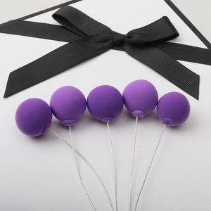 Five purple clay balloon cake toppers with flexible wires and black ribbon on white background