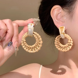 Detail of round rattan hoop earrings with beige marble resin studs on female model