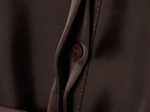 Vue détaillée du tissu de chemise en satin marron foncé avec bouton et texture soyeuse